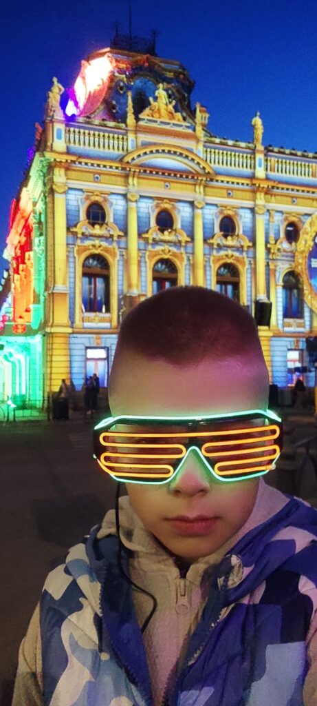 Szymon z 1 d - chłopiec w podświetlonych okularach stoi na tle podświetlonego Pałacu Poznańskiego