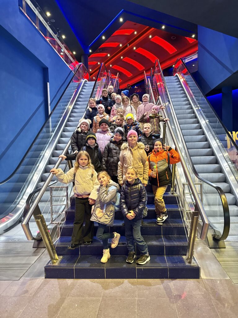 uczniowie z nauczycielem stoją między ruchomymi schodami w kinie