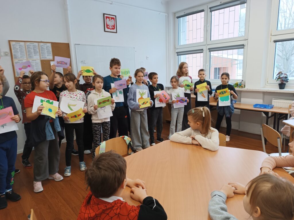 zdjęcie przedstawia grupę uczniów trzymających papierowe prace