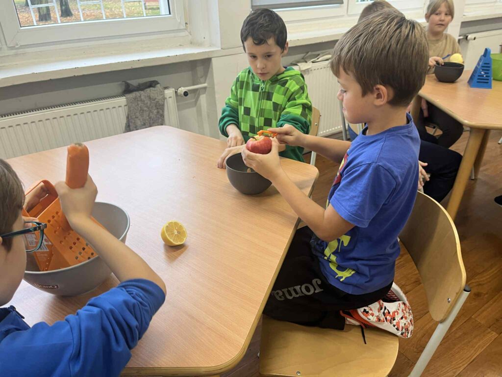 Chłopcy obierają jabłka przy stoliku.