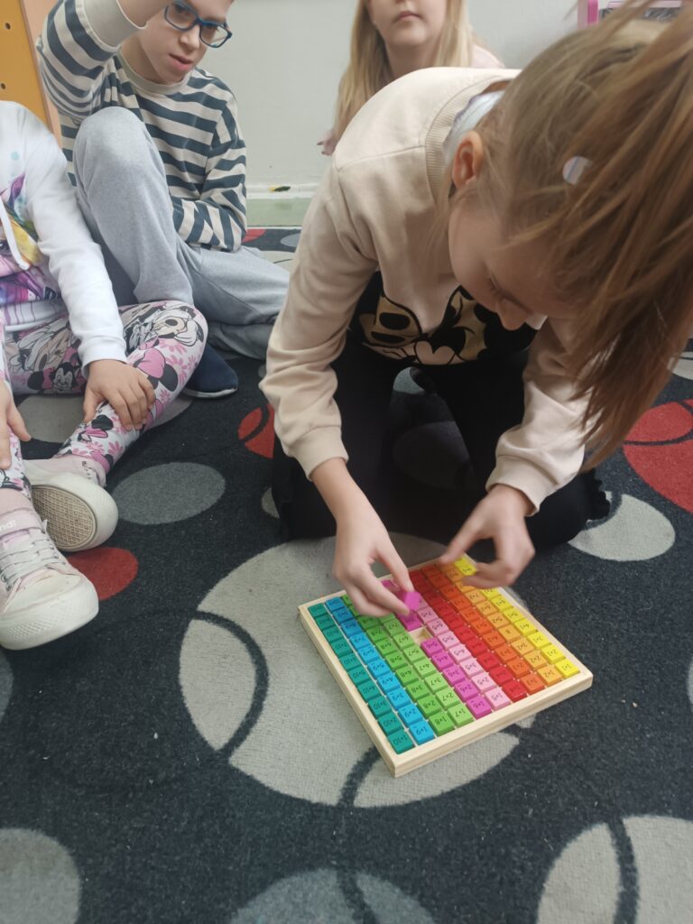 uczniowie rozwiązują zadania związane z tabliczką mnożenia na dywanie