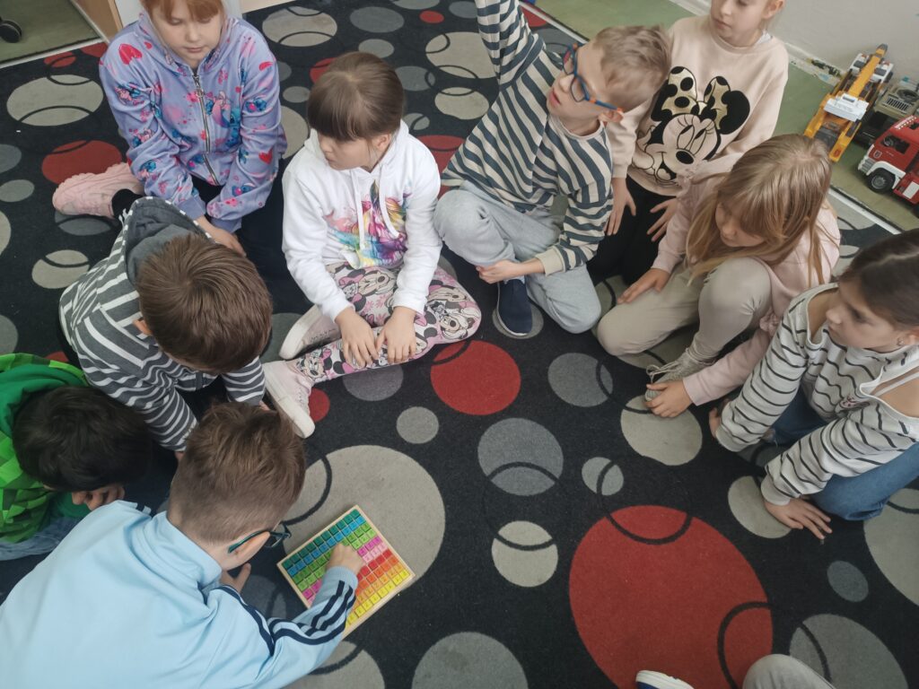 uczniowie rozwiązują zadania związane z tabliczką mnożenia na dywanie