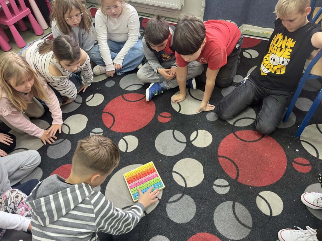 uczniowie rozwiązują zadania związane z tabliczką mnożenia na dywanie