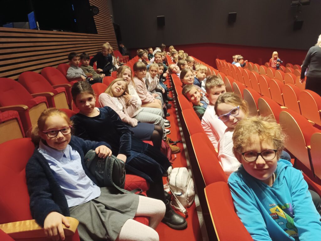 Uczniowie siedzą w rzędach czerwonych krzeseł