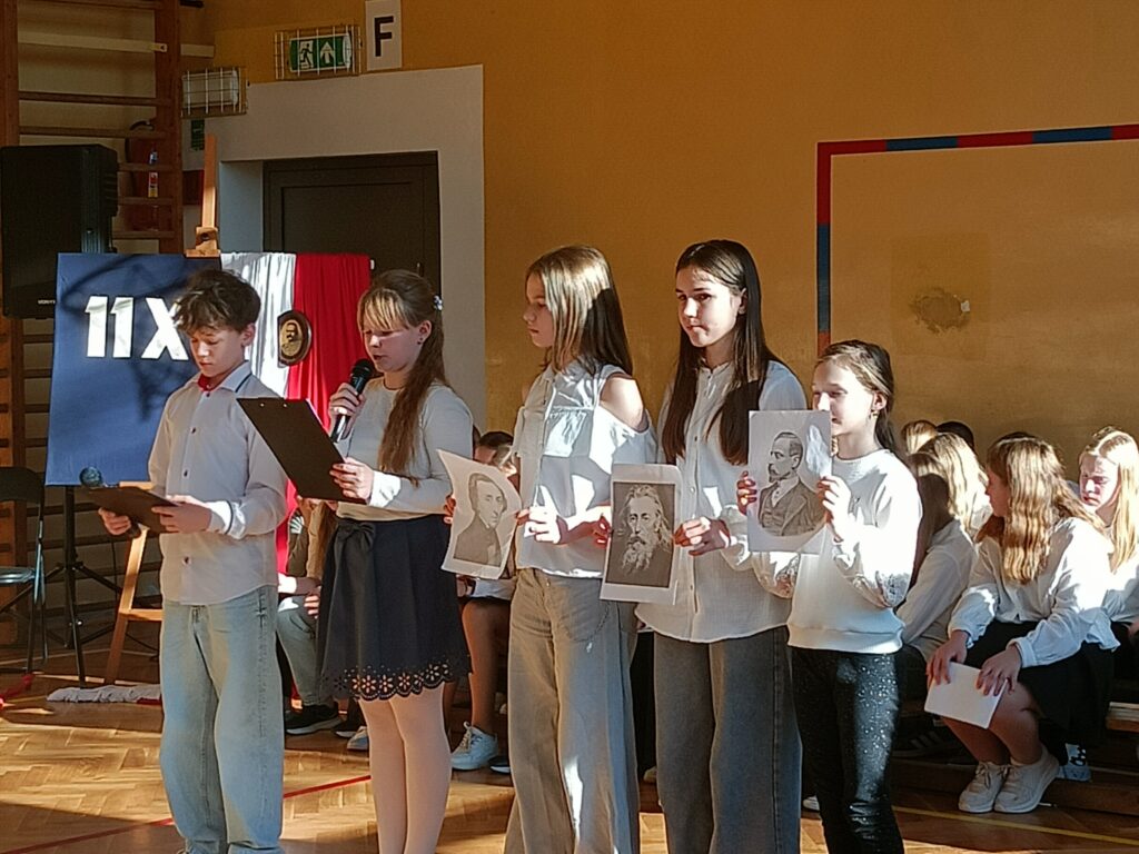 dzieci podczas apelu, trzymają zdjecia wybitnych polaków