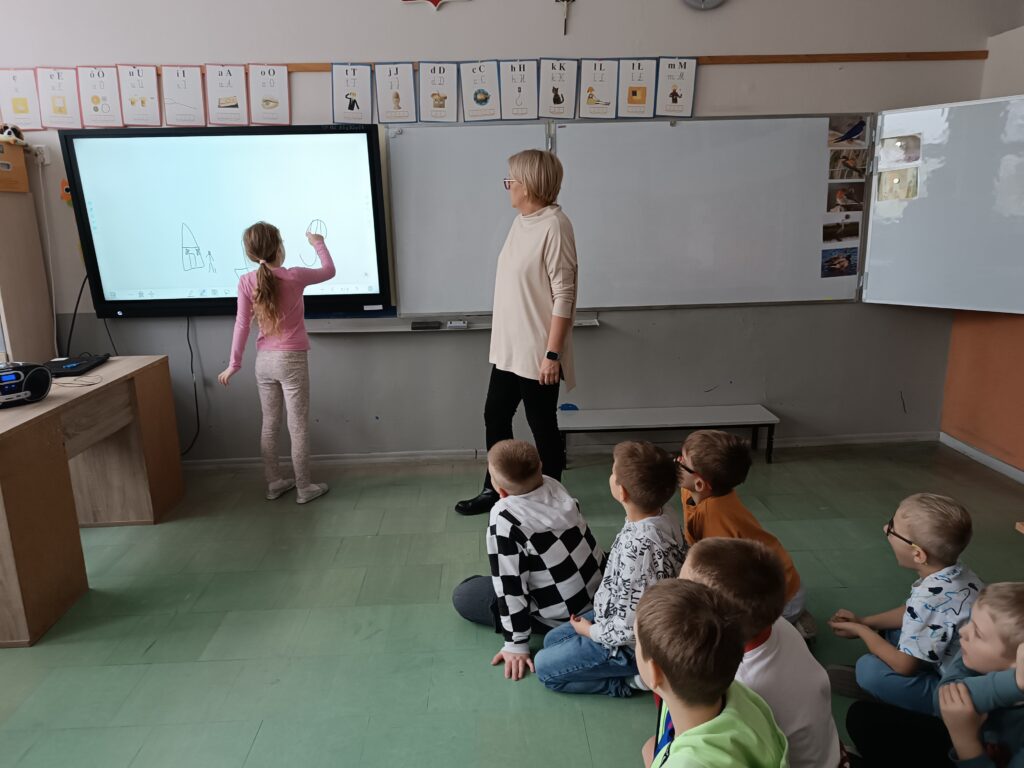 jeno z dzieci maluje na tablicy, reszta się przygląda