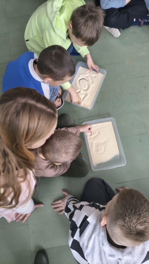 dzieci rysują palcem po piasku, piasek w pojemnikach plastikowych