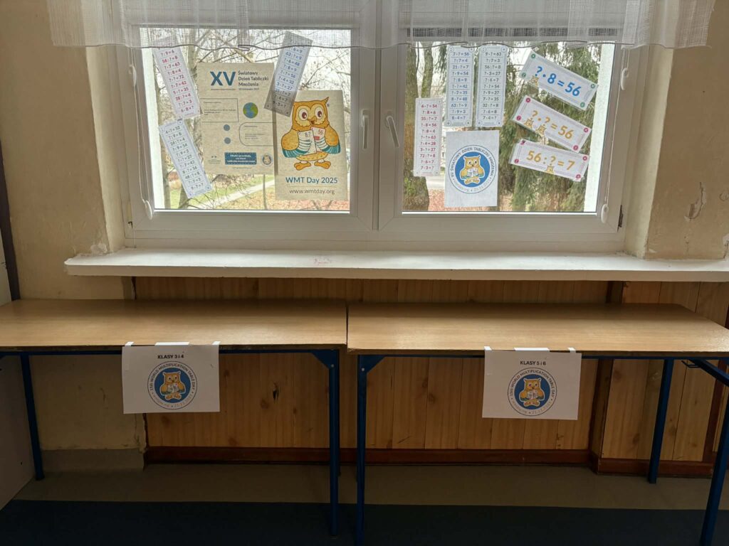 zdjęcie przedstawia naklejone plakaty na oknie szkoły związane z tabliczką mnożenia