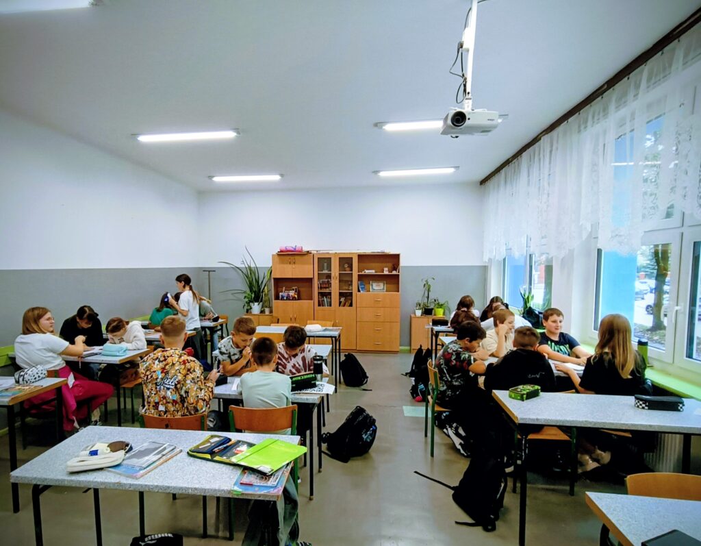 zdjęcie przedstawia uczniów siedzących w ławkach i wykonujących zadania.