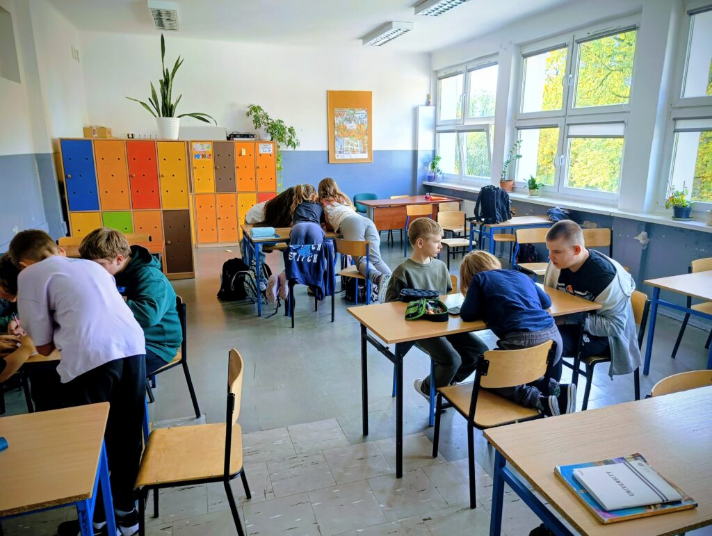 zdjęcie przedstawia uczniów siedzących w ławkach i wykonujących zadania.