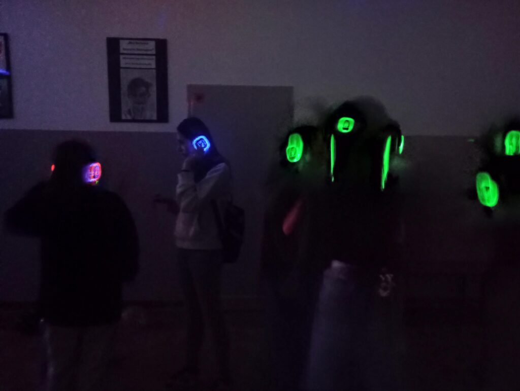 Uczniowie w świecących słuchawkach na głowach stoją w korytarzu w grupkach.