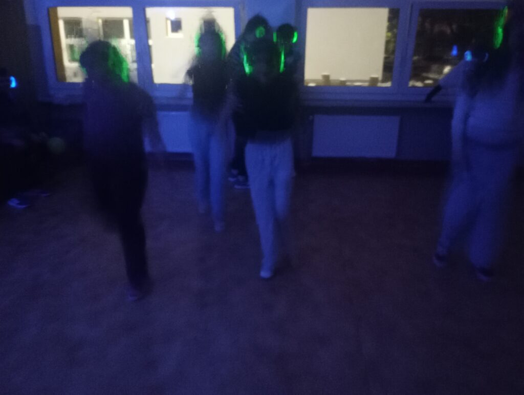 Dyskoteka. Uczniowie w świecących słuchawkach na głowach stoją w korytarzu w grupkach.