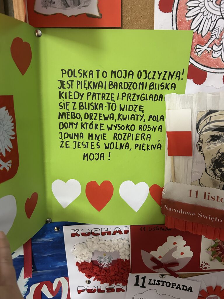 w środku zielonej kartki widnieje po lewej stronie godło Polski i serduszka, a po prawej wierszyk: Polska to moja ojczyzna!
