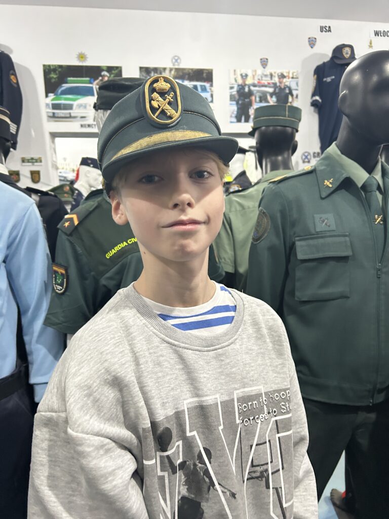 na pierwszym planie chłopiec ma zalożoną czapkę policjanta z Hiszpanii, na drugim planie manekiny w strojach policjantów z Hiszpanii