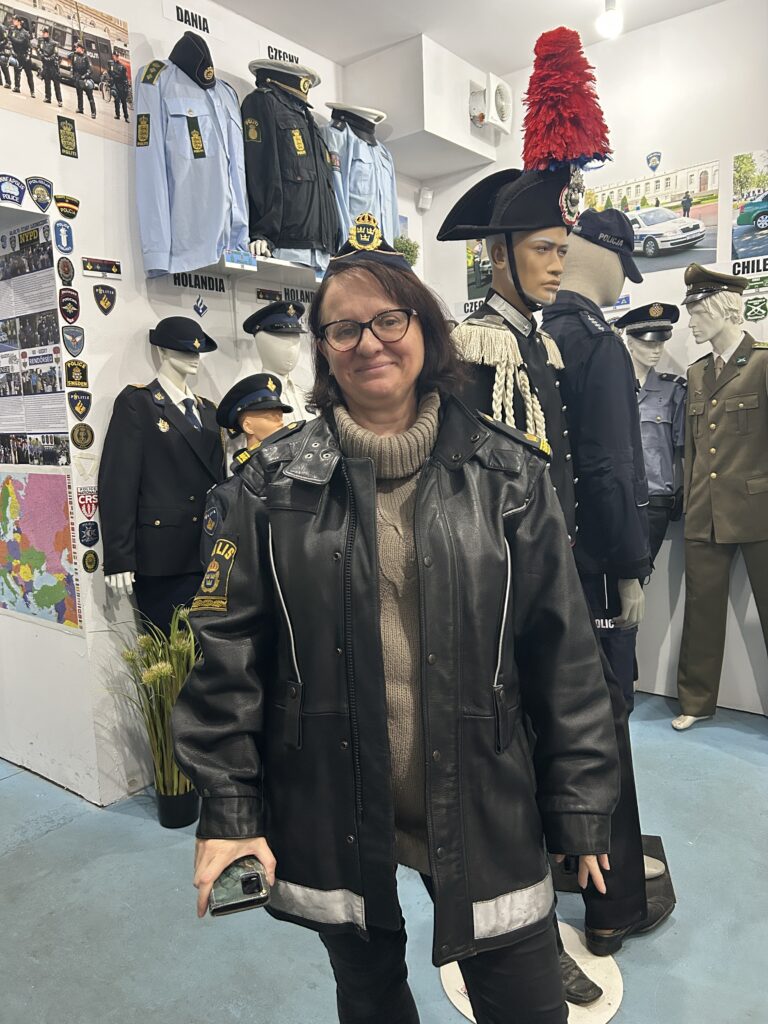 na pierwszym planie pani ubrana w skórzaną kurtkę policyjną