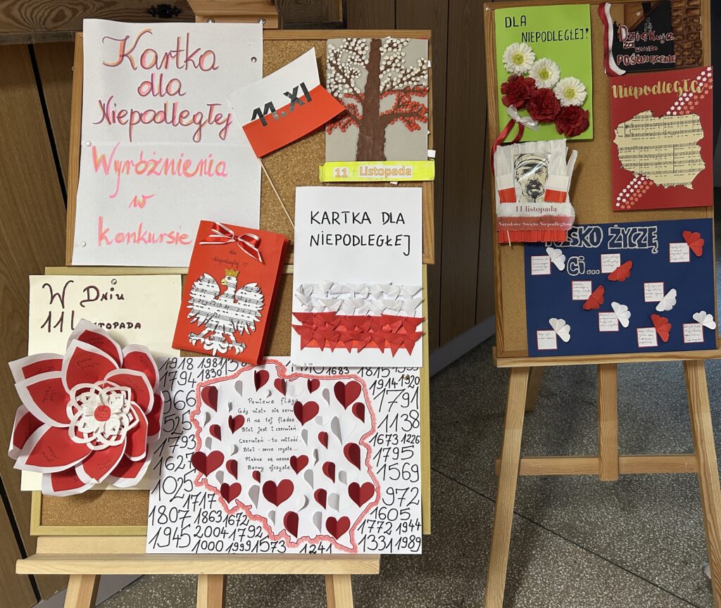 na dwóch sztalugach malarskich stoją tablice korkowe. Na jednej z nich napis: Kartka dla Niepodległej, Wyróżnienia w konkursie. Przypiętych jest 6 kartek. Widnieją na nich napisy, np. w dniu 11 listopada, kartka dla Niepodległej. Na kartkach są biało - czerwone barwy narodowe, na jednej z nich orzeł, jedna w kształcie flagi Polski, na innej jest drzewo z liśćmi biało czerwonymiNa drugiej tablicy wisi 5 kartek z napisami: Polsko życzę ci.., 11 listopada, dla Niepodległej, Niepodległa, dziękujemy za wasze poświęcenie. Na kartkach przyklejone kwiatki biało czerwone, portret Piłsudskiego, mapa Polski.