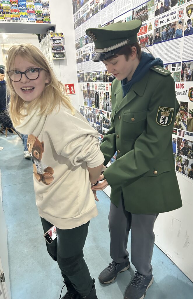 chłopiec ubrany w zielony mundur i czapkę niemieckiej policji zakłada dla zabawy na ręce kajdanki dziewczynce