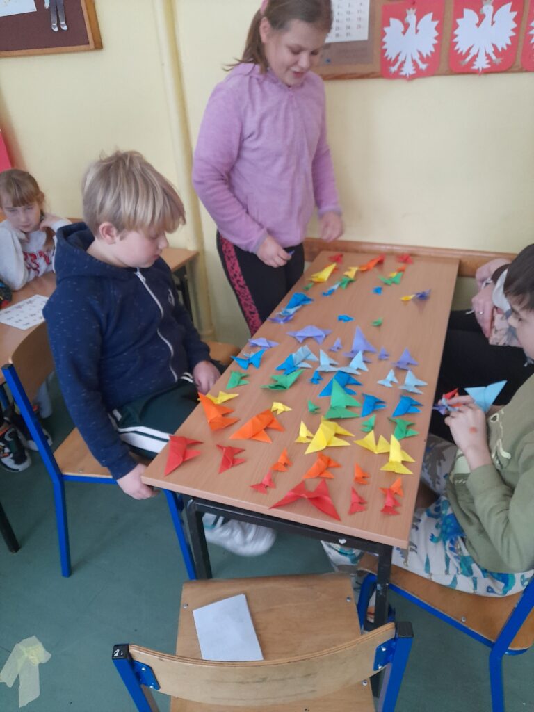 uczniowie siedzą przed stolikiem na którym są origami 