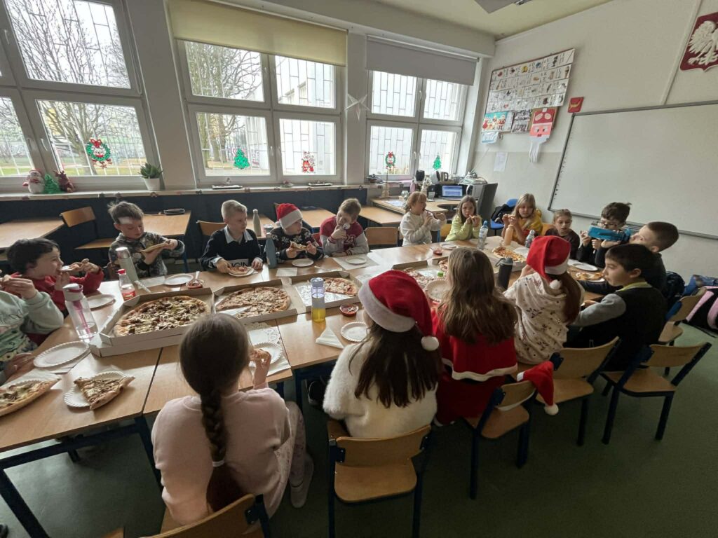 dzieci siedzą w ławeczkach i jedzą pizzę