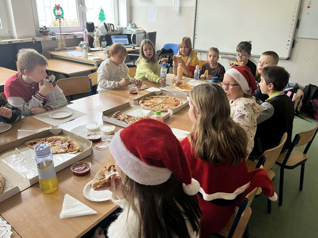 dzieci siedzą w ławeczkach i jedzą pizzę