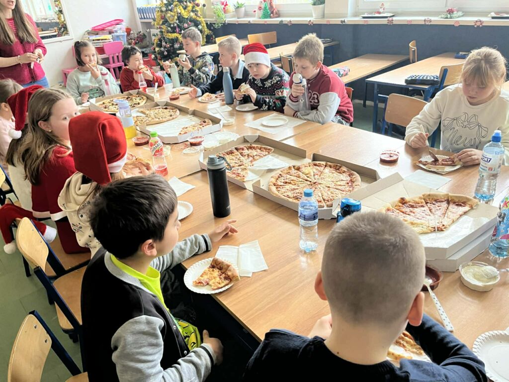 dzieci siedzą w ławeczkach i jedzą pizzę