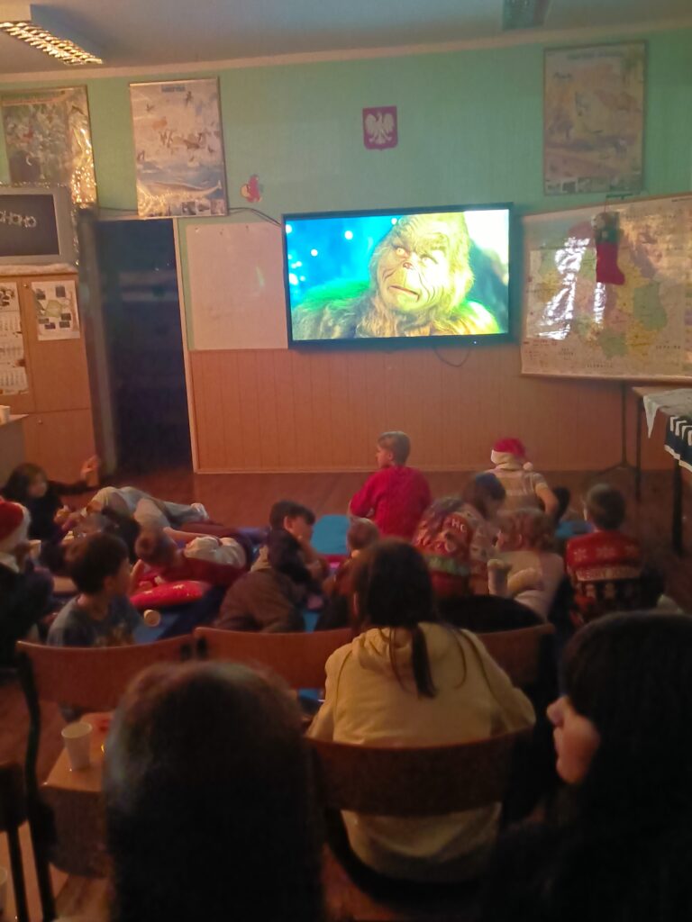 zdjęcie grupowe uczniów siedzących na krzesłach, w oddali film na ekranie interaktywnym