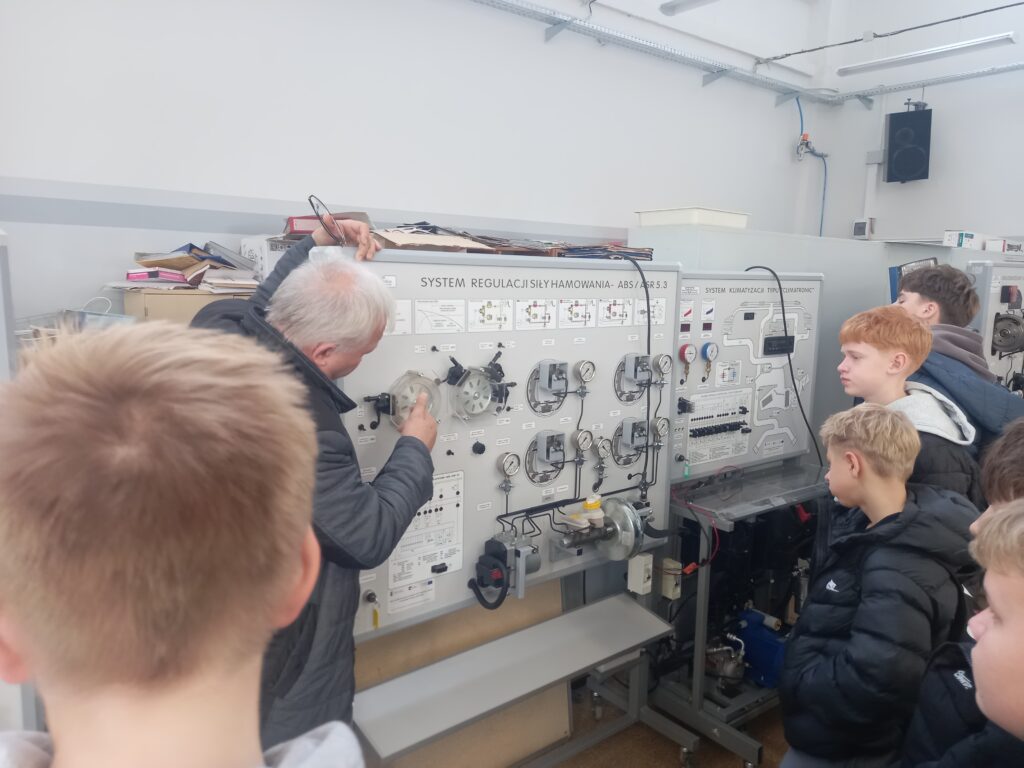 mężczyzna tłumaczy działanie maszyny dzieciom 