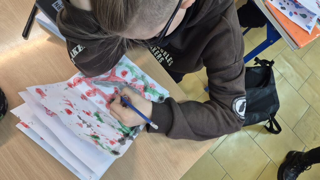 Uczeń siedzący w ławce i robiący kleksy na białych kartkach