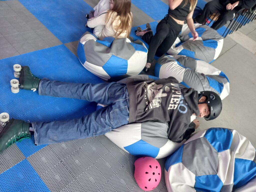 uczeń leży na poduszce, ma na stopach wrotki. Obok są inne dzieci.
