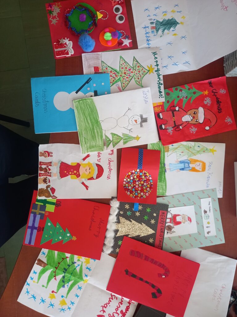 świąteczne kartki wykonane przez dzieci, choinki, mikołaje, napisy po angielsku.