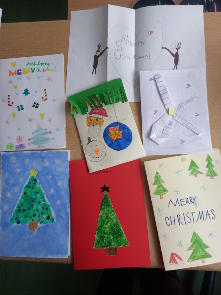 świąteczne kartki wykonane przez dzieci, choinki, mikołaje, napisy po angielsku.