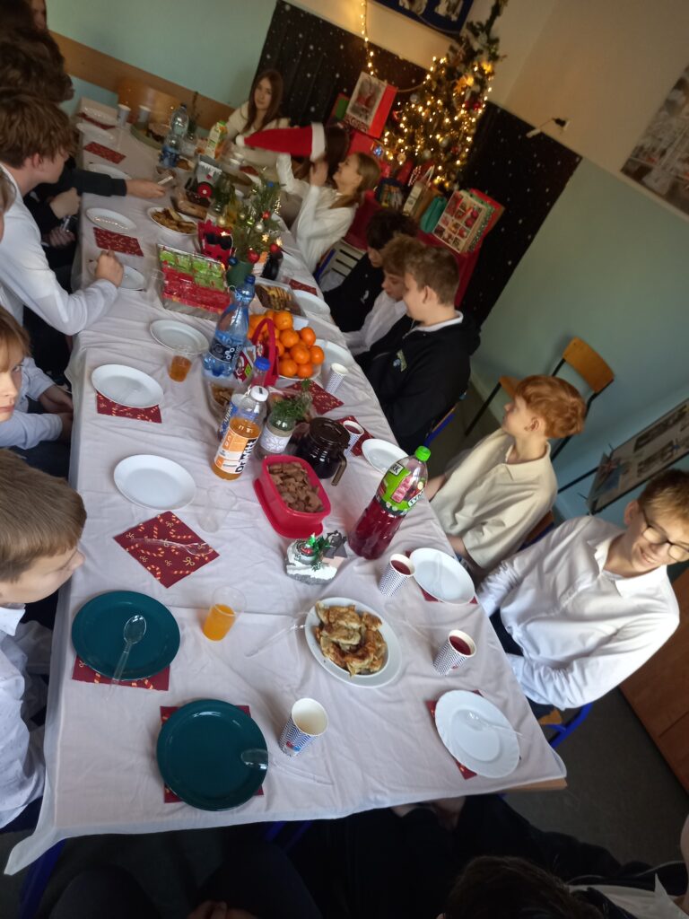 jedzenie i talerzyki rozłożone na ławkach przykryte białym obrusem, przy stolikach siedzą uczniowie