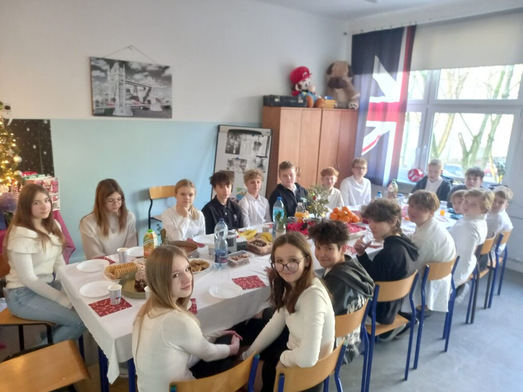 jedzenie i talerzyki rozłożone na ławkach przykryte białym obrusem, przy stolikach siedzą uczniowie