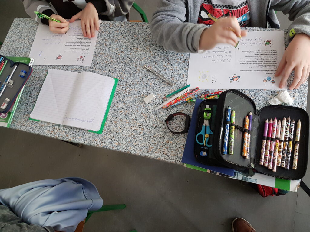 Zdjęcie pokazuje uczniów w klasie przy stolikach, przygotowujących kartki związane z inicjatywą edukacyjną miasta.