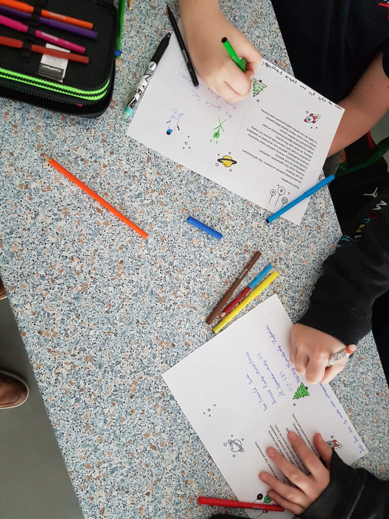 Zdjęcie przedstawia uczniów kolorujących świąteczne przesłanie dla akcji wspierającej ESA w Łodzi.