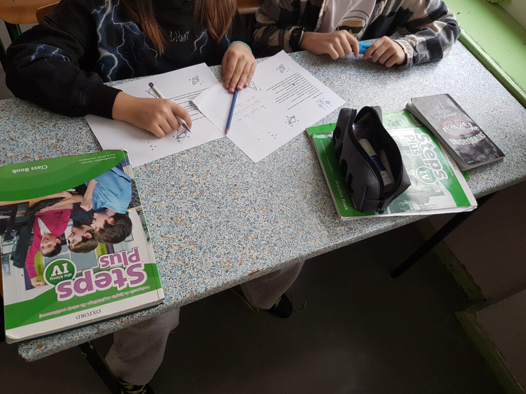 Zdjęcie przedstawia uczniów wypełniających świąteczne kartki marzeń o rozwoju nauki i technologii w Łodzi.