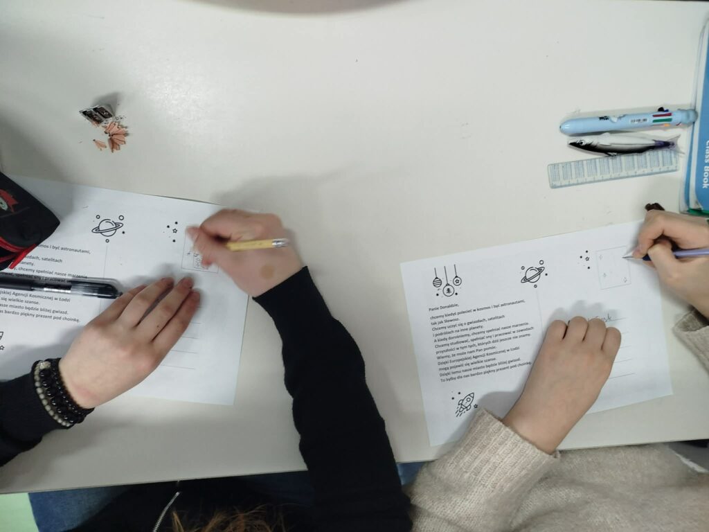 Na zdjęciu widoczne są dłonie uczniów wypełniających kartki świąteczne do Prezesa Rady Ministrów.