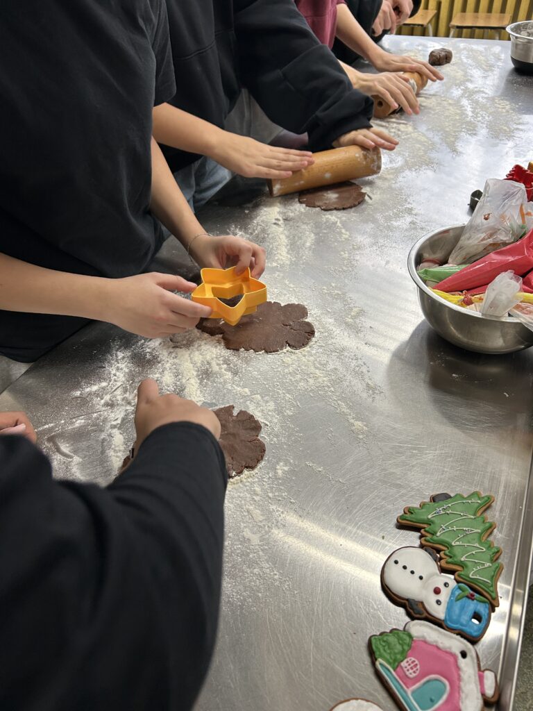 na stole widać ręce i z małych kawałków ciasta dzieci wykrawają formami pierniczki
