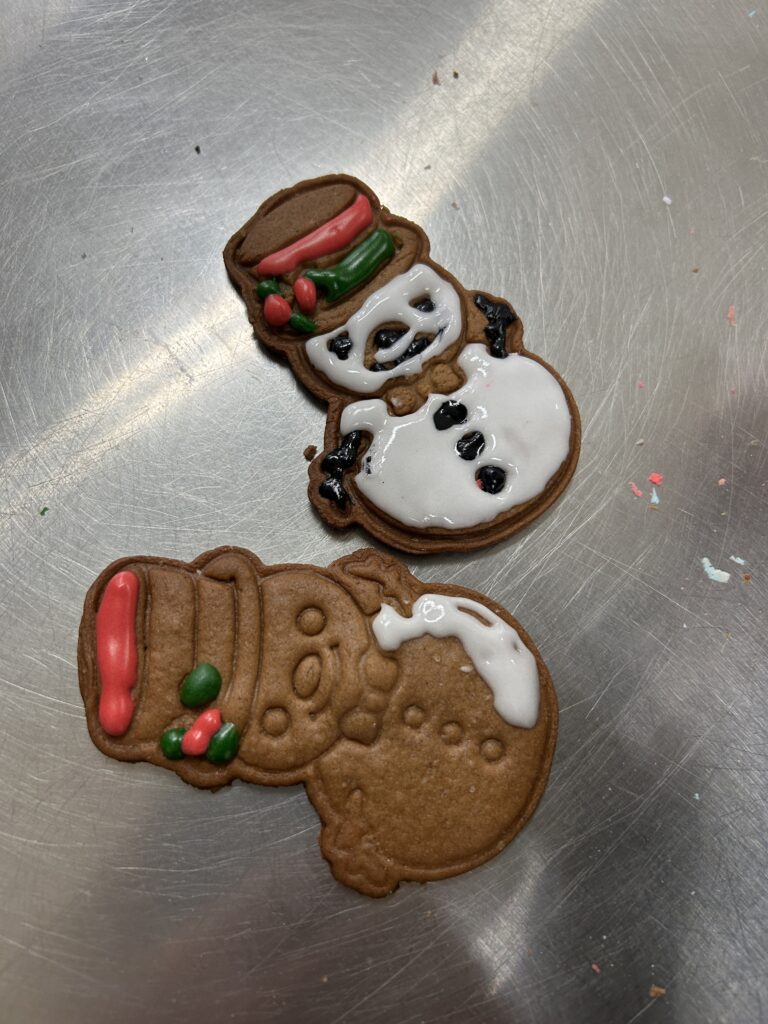 na stole leżą dwa cisteczka-pierniki - dwa bałwanki, jeden udekorowany kolorowym lukrem, drugi ozdobiony lukre w małej części