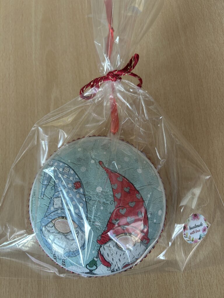 zapakowana w przezroczystą folię i zawiązana kolorową wstążeczką bombka , a na niej dwa kolorowe skrzaty