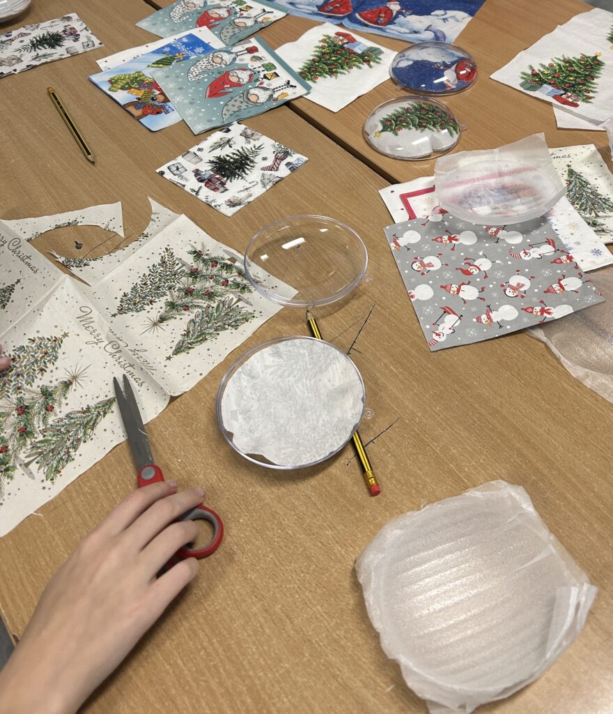 na ławkach leżą kolorowe serwetki, część jest już wycięta i dopasowana do wnętrza bombek