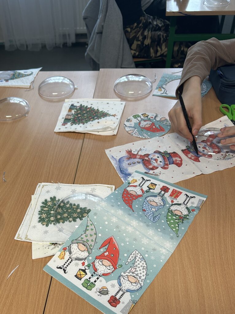 na ławkach leżą świąteczne serwetki papierowe. Widać rękę chłopca, który odrysowuje na serwetce koło