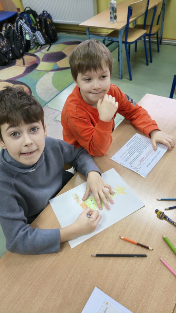 dwoje chłopców, jeden maluje choinkę, drugi trzyma kartkę z tekstem