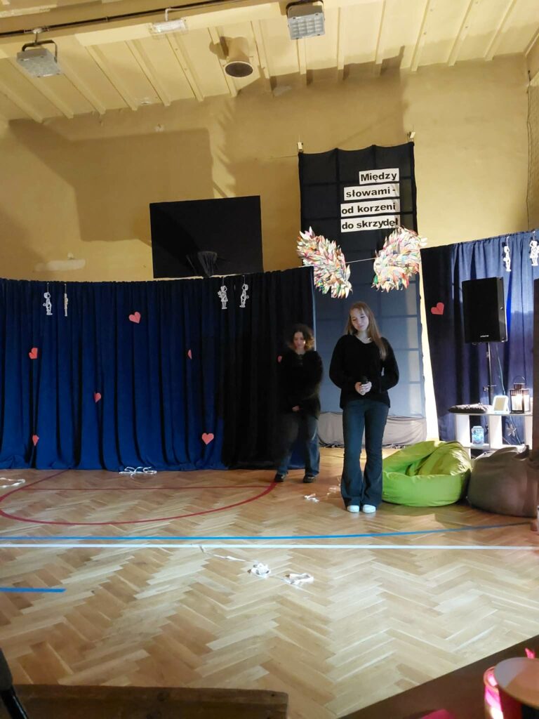 uczennica podczas przedstawienie, za nią wystrój z napisem między słowami od korzeni do skrzydeł 