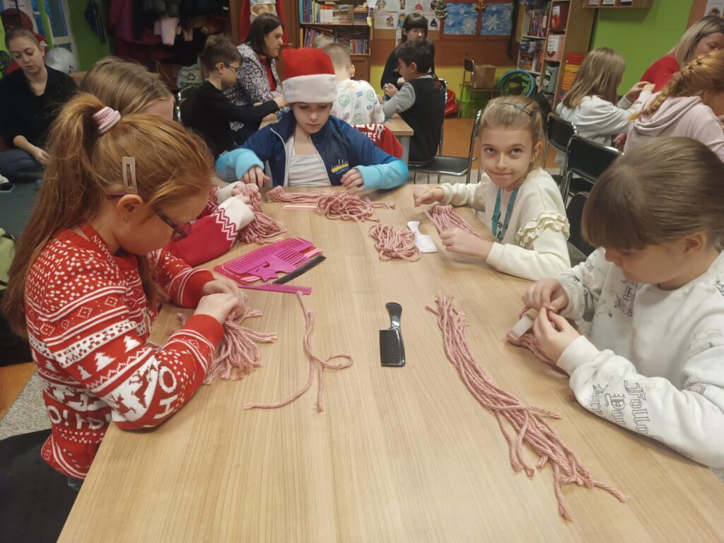 Uczniowie podczas warsztatów przy stoliku wykonują pracę z wykorzystaniem włóczki 