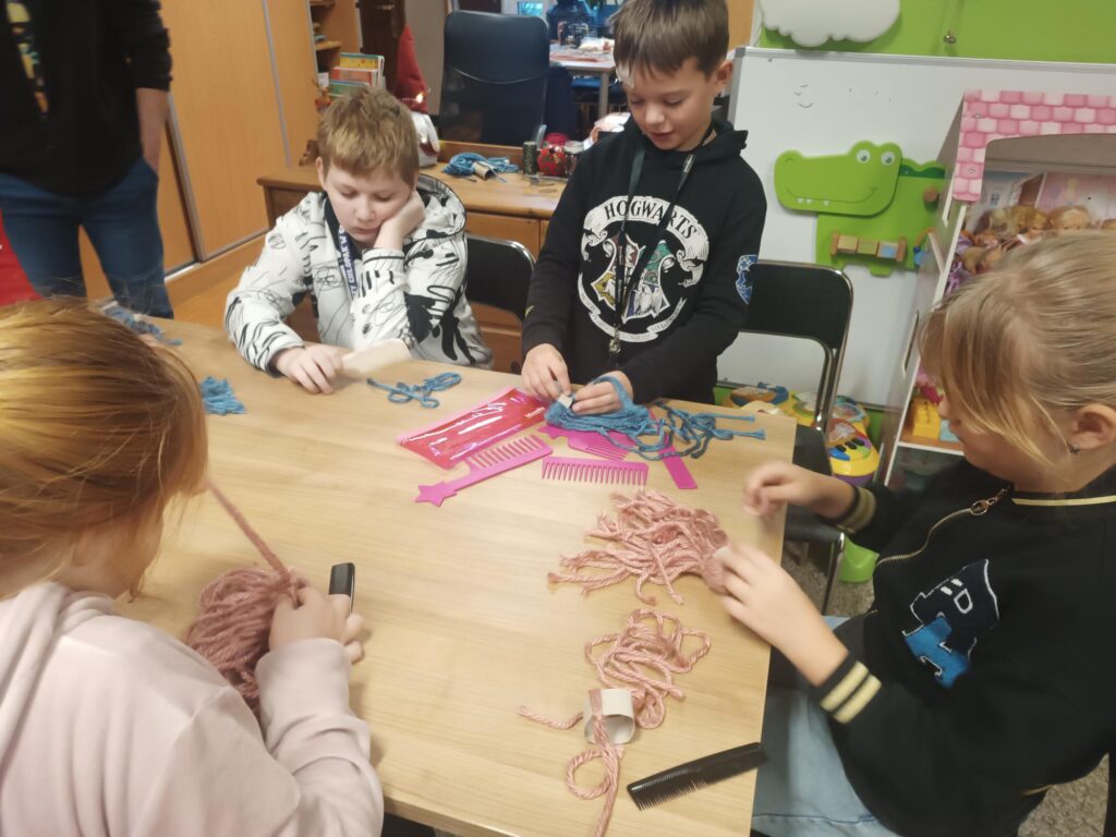 Uczniowie podczas warsztatów przy stoliku wykonują pracę z wykorzystaniem włóczki 