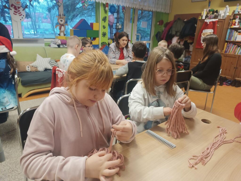 Uczniowie podczas warsztatów przy stoliku wykonują pracę z wykorzystaniem włóczki 