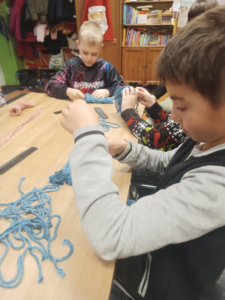 Uczniowie podczas warsztatów przy stoliku wykonują pracę z wykorzystaniem włóczki 