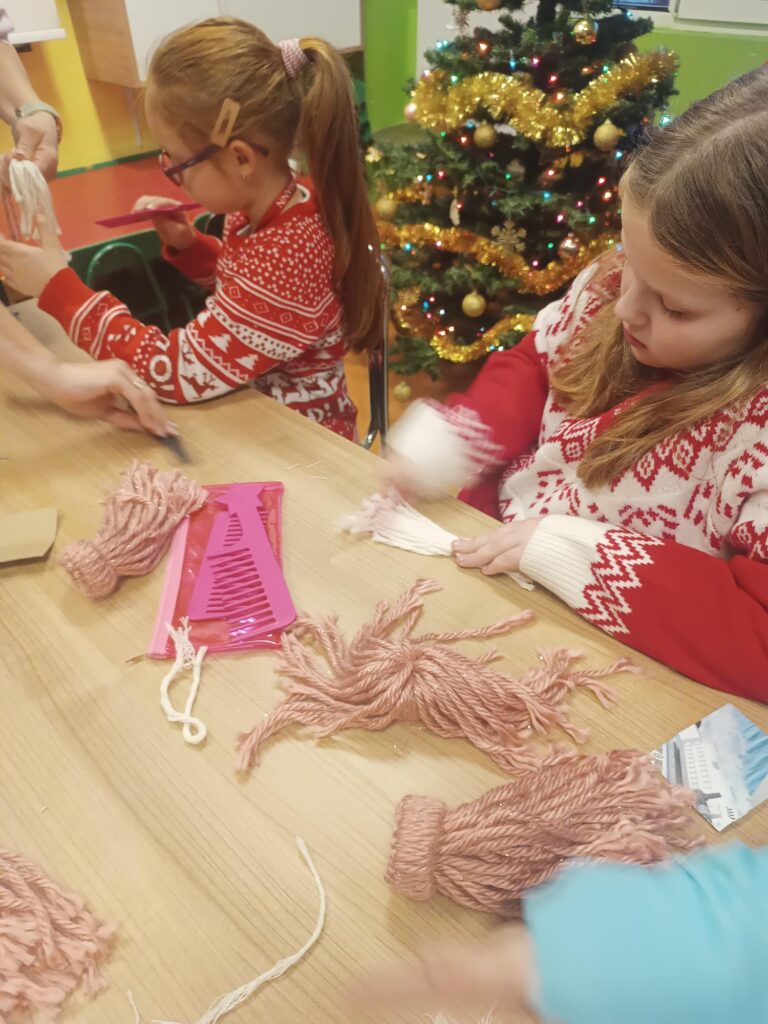 Uczniowie podczas warsztatów przy stoliku wykonują pracę z wykorzystaniem włóczki 