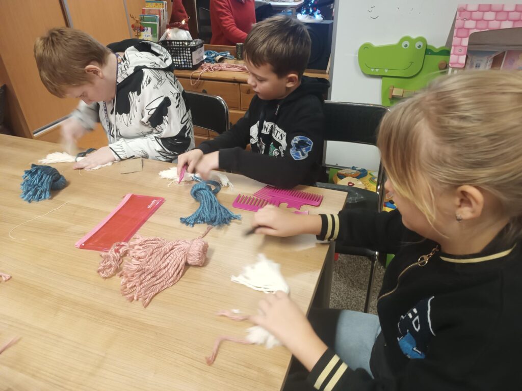 Uczniowie podczas warsztatów przy stoliku wykonują pracę z wykorzystaniem włóczki 